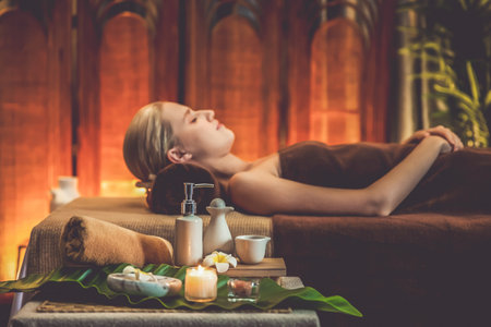 Aromatherapy massage ambiance or spa salon composition setup with focus decor candles and spa accessories on blurred woman enjoying blissful aroma spa massage in resort or hotel background. Quiescentの写真素材