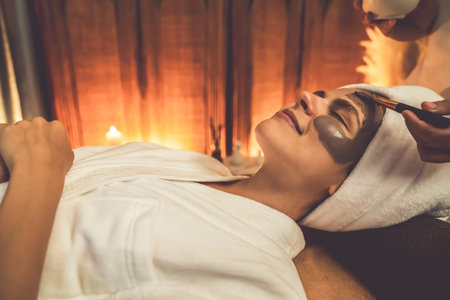 Serene ambiance of spa salon, woman customer indulges in rejuvenating with charcoal face cream massage with warm lighting candle. Facial skin treatment and beauty care concept. Quiescentの写真素材