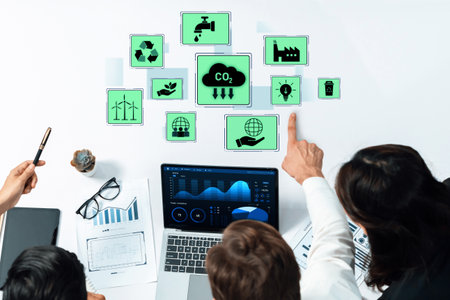 A diverse business team focuses on environmental data displayed on laptops and tablets, highlighting sustainability metrics and collaboration in innovative settings.の写真素材