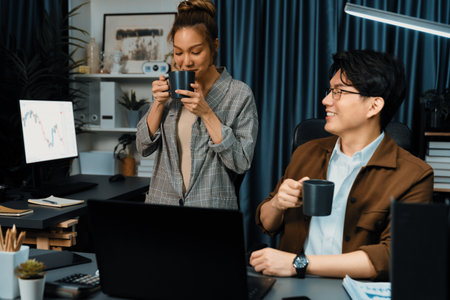 Sales managers discussing while drinking coffee cup together at over late night at home office, concept of modern working place with business report at breaking time with coworker at desk. Infobahn.の写真素材
