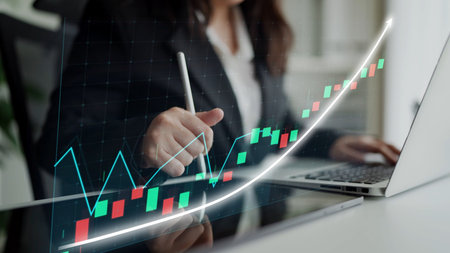 A business professional diligently analyzes financial data on a laptop, working in a modern office environment with market growth graphs, showcasing strategic insights.の写真素材