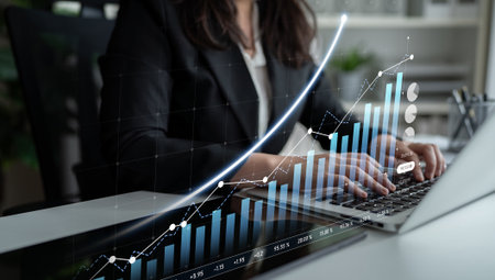 A business professional intently analyzing financial data on a laptop, featuring graphs that depict growth trends, set within a modern office environment.の写真素材