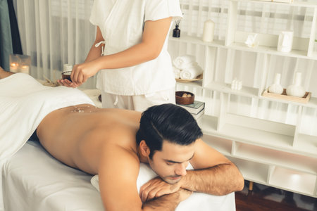 Blissful man customer having exfoliation treatment in luxury spa salon with warmth candle light ambient. Salt scrub beauty treatment in health spa body scrub. Quiescentの写真素材