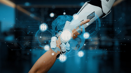 A robotic hand connects with a human hand in a modern workspace, symbolizing the merging of...