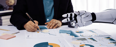 A human writer collaborates with a robotic hand in an office setting, analyzing charts and data. This image represents the future of technology and teamwork.の写真素材