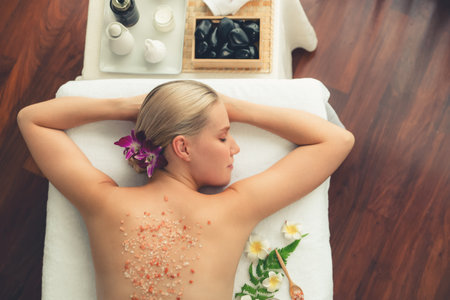 Panorama top view woman customer having exfoliation treatment in luxury spa salon with warmth candle light ambient. Salt scrub beauty treatment in health spa body scrub. Quiescentの写真素材