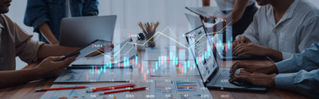 A modern office scene showing a team engaged in financial data analysis, utilizing laptops, charts,...