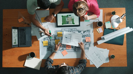Top down view of civil engineer handed document while looking at blueprint. Aerial view of architect team brainstorming idea and planning building design while sitting at table with plan. Symposium.の写真素材