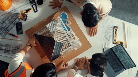 Top view of skilled architect designer team using pencil measuring house model. Group of civil engineer planning and designing blueprint while pointing at building at table with laptop.の写真素材