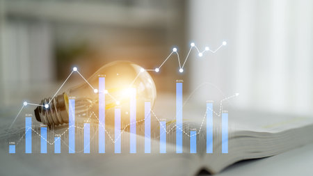 A close-up image featuring a glowing light bulb alongside business growth analytics displayed on an open book, emphasizing creativity and knowledge in entrepreneurship.の写真素材