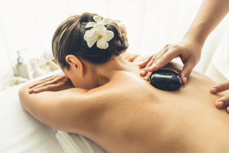 Hot stone massage at spa salon in luxury resort with day light serenity ambient, blissful woman customer enjoying spa basalt stone massage glide over body with soothing warmth. Quiescentの写真素材