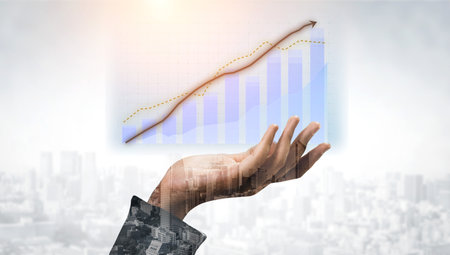 A hand emerges in the foreground, symbolizing ambition and growth, while a graph highlights an upward trend against a soft city background.の写真素材