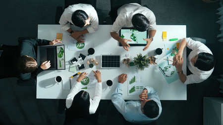 Top down view of business team discussing about using clean energy and sustainable investment at meeting table with wind mill, document with environmental graph and wooden house model.の写真素材