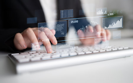 A focused business professional types on a keyboard while visualizing digital financial graphs and charts, emphasizing the importance of technology in finance and decision-making.の写真素材