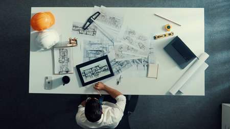 Top down view of engineer looking at tablet while checking building material at paper or document. Aerial view of skilled architect designing house construction while looking at blueprint.の写真素材