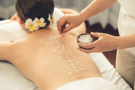 Woman customer having exfoliation treatment in luxury spa salon with warmth candle light ambient. Salt scrub beauty treatment in health spa body scrub. Quiescentの写真素材