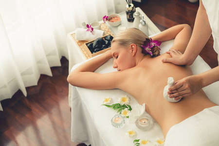 Hot herbal ball spa massage body treatment, masseur gently compresses herb bag on woman body. Tranquil and serenity of aromatherapy recreation in day lighting ambient at spa salon. Quiescentの写真素材