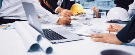 A diverse group of professionals engaged in collaborative planning over construction documents in a...
