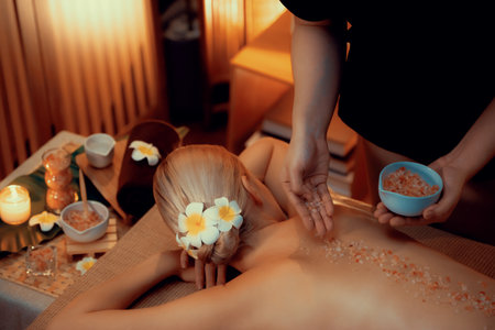 Woman customer having exfoliation treatment in luxury spa salon with warmth candle light ambient. Salt scrub beauty treatment in Health spa body scrub. Quiescentの写真素材