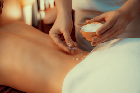 Woman customer having exfoliation treatment in luxury spa salon with warmth candle light ambient. Salt scrub beauty treatment in Health spa body scrub. Quiescentの写真素材