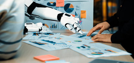 A robotic hand collaborates with a human in analyzing data charts and graphs, showcasing modern technology's role in business data visualization and teamwork.の写真素材