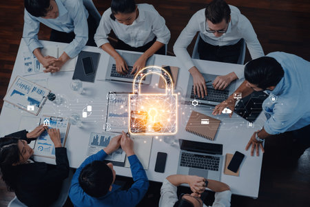 A diverse team meets around a table with laptops and documents, discussing data security highlighted by a digital lock graphic, emphasizing the importance of information protection.の写真素材