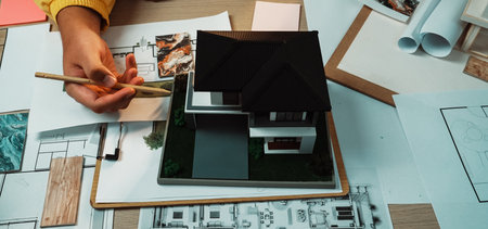 A creative workspace featuring hands working on an architectural model, surrounded by sketches, blueprints, and design tools, showcasing the design process.の写真素材