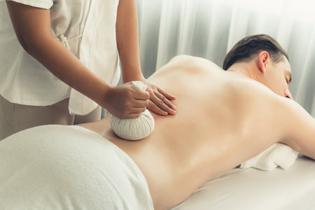 Hot herbal ball spa massage body treatment, masseur gently compresses herb bag on man body. Tranquil and serenity of aromatherapy recreation in day lighting ambient at spa salon. Quiescentの写真素材