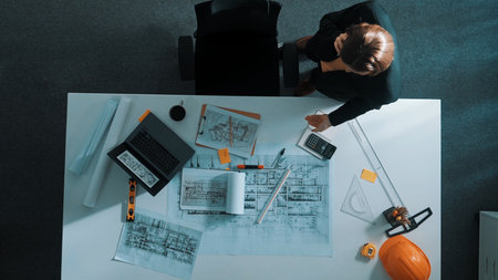 Top view of civil engineer talking to manager by using phone while holding calculator and standing at meeting room. Aerial view calling architect and talking about building structure.の写真素材