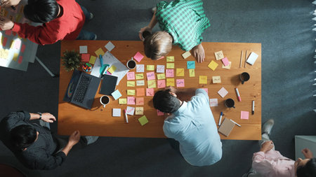 Top view of skilled business people discuss plan at meeting room while writing idea at sticky notes and stick at whiteboard. Group of diverse team working together to planning strategy. Convocation.の写真素材