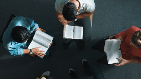 Top down view of prayer reading at bible book and sitting in circle with bible book on laps. Aerial view of diverse people looking at book while studying with faith, trust and hope, calm. Symposium.の写真素材