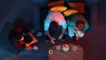 Top aerial view of happy father, mother, and colleague watching a movie together while drinking fizzy water. Happy family spending time together while sitting in a cozy living room at night.の写真素材