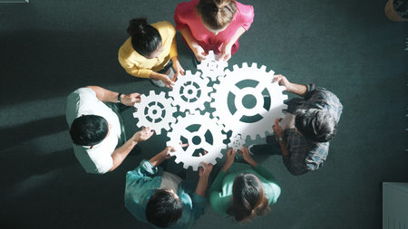 Top down aerial view of business team working together to gather cog together. Aerial view of professional diverse group holding cog and complete white gear. Represented unity, teamwork. Symposium.の写真素材