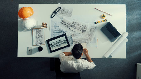 Time lapse of skilled engineer sitting at table and looking at tablet while checking building material. Top down view of architect design house construction while looking at blueprint.の写真素材