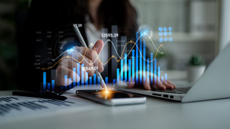 A professional woman conducts financial analysis using a digital tablet and laptop, showcasing charts and graphs in a modern office setting for effective business decision-making.の写真素材
