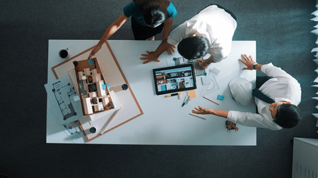 Time lapse of designer looking at model while discussing about building. Top view of architect engineer explaining idea while talking and writing blueprint scattering at meeting table.の写真素材