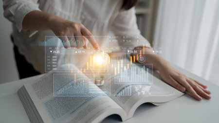 A person engages with an open book, showcasing digital charts and a glowing light bulb, symbolizing the fusion of knowledge and innovative ideas for business growth.の写真素材