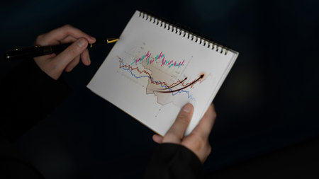 A close-up view of hands holding a sketchbook displaying colorful graphs and charts, symbolizing data analysis and financial insights in a creative environment.の写真素材