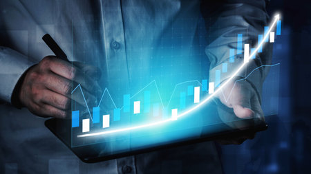 A business professional uses a digital tablet to analyze financial data with a graphical...