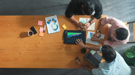 Top view of skilled project manager talking about financial graph to investors while sitting at meeting table with data analysis document. Diverse team discussing and brainstorming idea.の写真素材