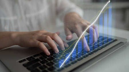 A person typing on a laptop keyboard while interactive digital graphs symbolize growth and data...