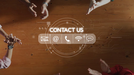 A top view of hands gathering around a wooden table with a digital Contact Us graphic that...