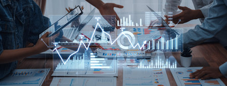 Business professionals engage in discussion while analyzing data trends through digital graphs in a modern office. Collaborative efforts drive strategy and performance improvements.の写真素材