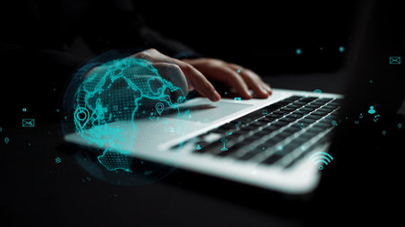 A close-up image of hands typing on a laptop, featuring a digital globe and communication icons, illustrating modern technology and remote work concepts vividly.の写真素材