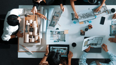 Top aerial view business people brainstorming about building interior at table with house model and laptop displayed house plan while architect engineer drawing and writing at blueprint.の写真素材