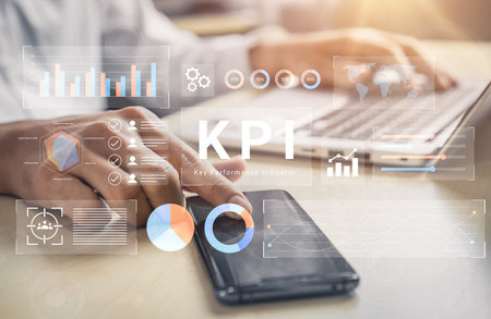 A business professional engages in data analysis using key performance indicators on a mobile device and laptop, highlighting important insights and trends.の写真素材