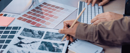 A modern workspace features hands examining color swatches and design materials. A functional setup includes a keyboard, reflecting creativity in the design process.の写真素材