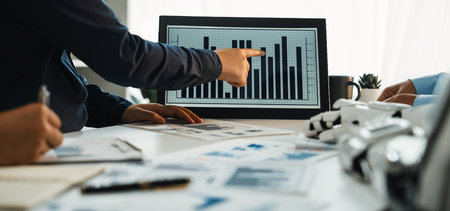 A professional business team collaborates in a modern office, analyzing graphs and charts displayed...