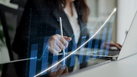 A businesswoman reviews data trends on her laptop, using a digital graph visualization. This scene...
