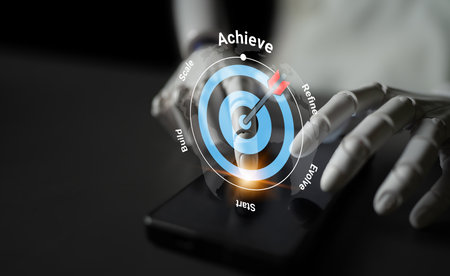 A sleek smartphone lies on a surface with a futuristic hand interacting with a digital achievement target, symbolizing goal setting and personal growth.の写真素材